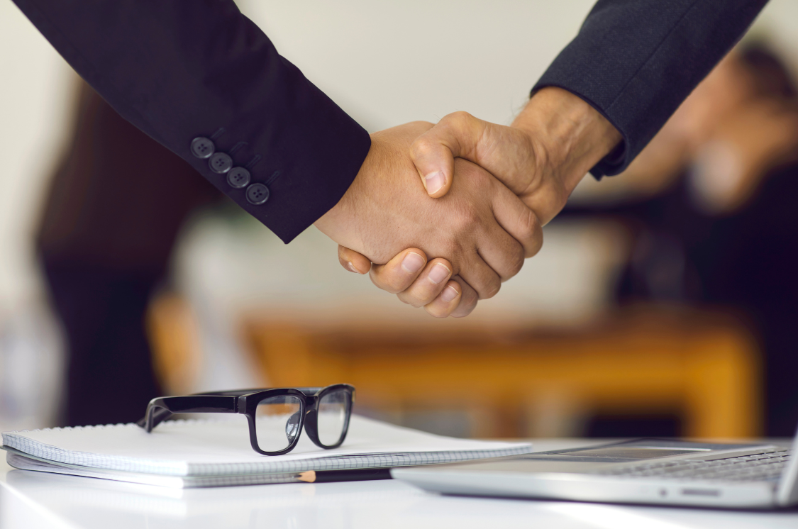 Handshake between professionals over a desk, symbolizing partnership, HR strategy, and impact.