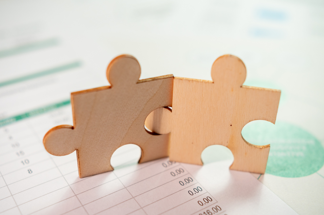 Two puzzle pieces fitting together over a spreadsheet, symbolizing strategic alignment in business.