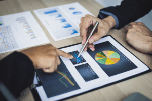 Two senior executives analyzing financial performance charts on a clipboard, pointing with a pen and finger to discuss data for corporate strategy.