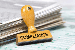 Wooden stamp with the word Compliance placed on financial documents and reports, symbolizing corporate compliance, regulation, and risk management.