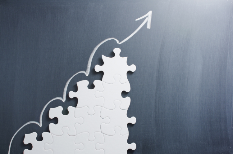 Puzzle pieces fit together to form the base of a hand-drawn arrow pointing up, symbolizing the journey from experience to innovation and how experts foster business growth.