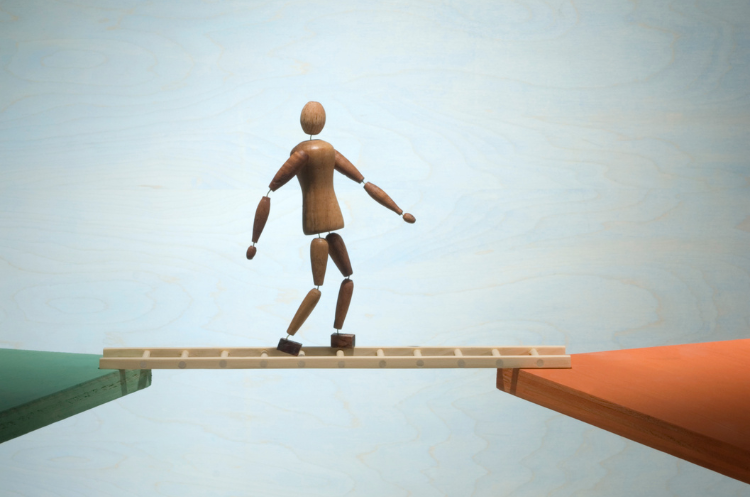 A wooden figurine carefully balances on a plank, bridging a gap to symbolize a successful career transition after 50.