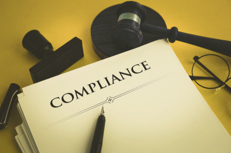 A desk scene showing a 'COMPLIANCE' document, a gavel, and glasses, illustrating an expert career guide and job outlook for a Compliance Specialist.