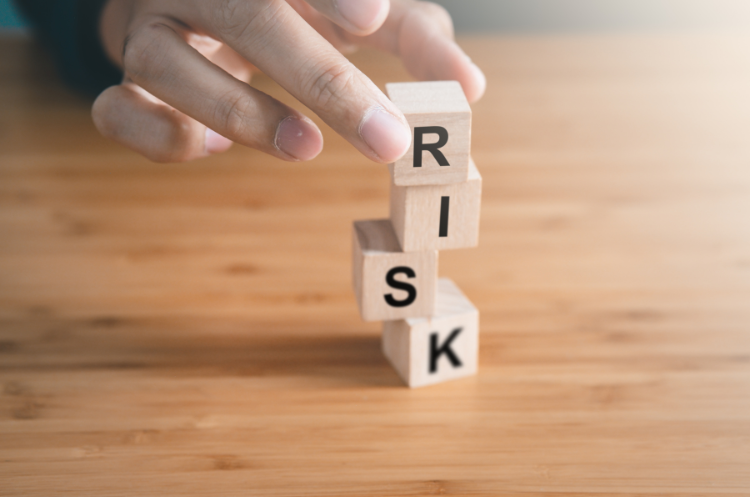 A hand stacking wooden blocks spelling the word RISK to represent the role and responsibilities of a Chief Risk Officer (CRO)