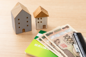 Miniature wooden houses placed next to Japanese Yen banknotes and a bank passbook, symbolizing home financing and mortgage planning for professionals in Singapore
