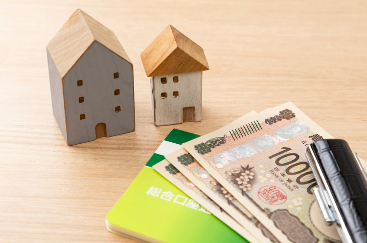Miniature wooden houses placed next to Japanese Yen banknotes and a bank passbook, symbolizing home financing and mortgage planning for professionals in Singapore