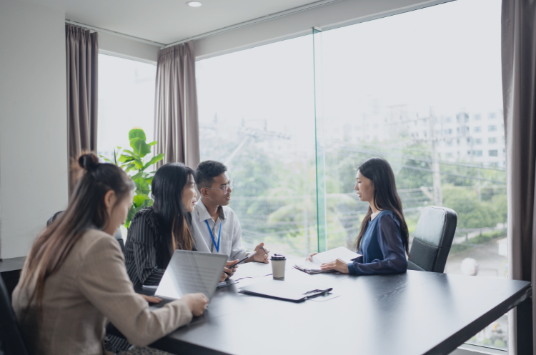 A group of diverse business professionals in a modern Singapore office setting engaged in a consulting meeting. Senior professionals and consultants discussing strategy around a conference table with laptops, illustrating career development in the Singapore consulting industry.