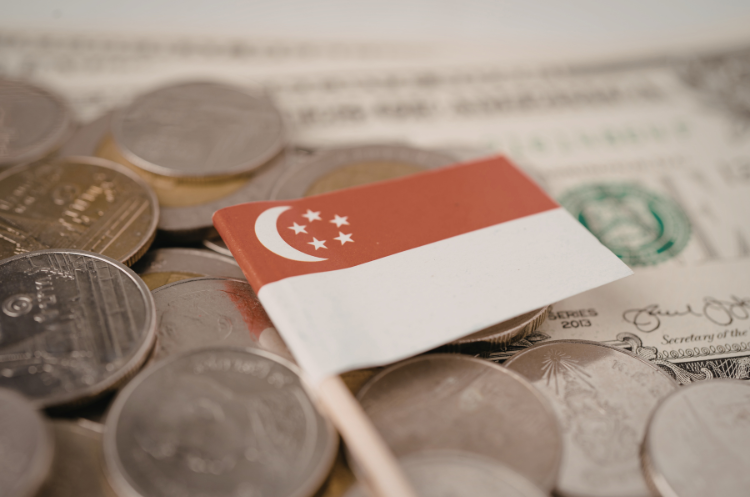 A small Singapore flag resting on a pile of coins and banknotes, symbolizing the financial services sector. This imagery represents the career path of a financial consultant in Singapore and the local wealth management industry.