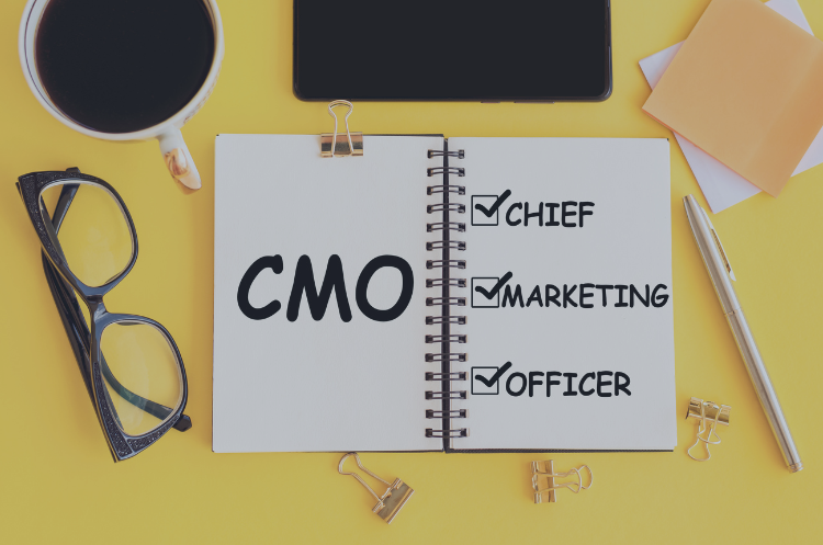 Fractional CMO concept with notebook showing Chief Marketing Officer checklist and workspace items on desk.