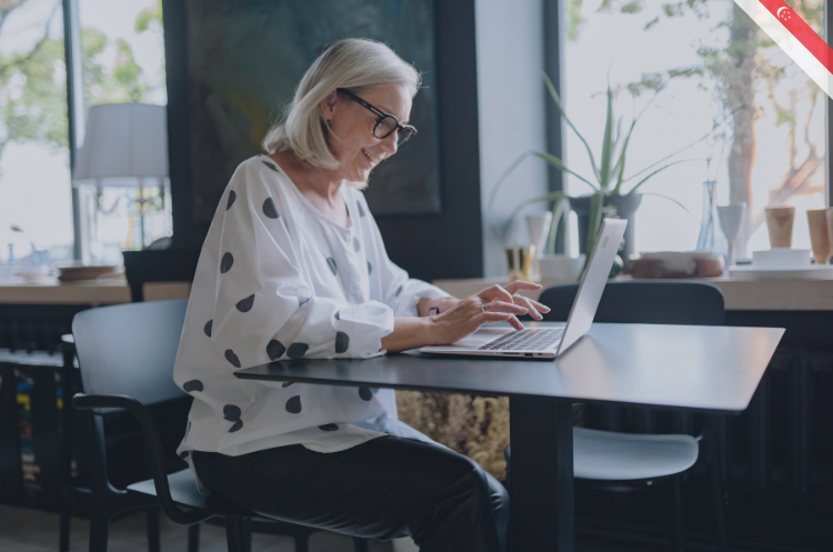 A smiling senior woman working on a laptop in a cafe, illustrating how to find work after retirement in Singapore.