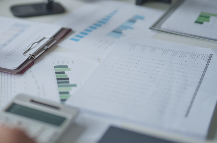 A desk covered in financial reports, bar charts, and data analytics papers, with a calculator in the foreground. This visual emphasizes the strategic analysis, revenue management, and performance tracking essential to the role of a Key Account Director in driving business growth and maintaining high-value client relationships.