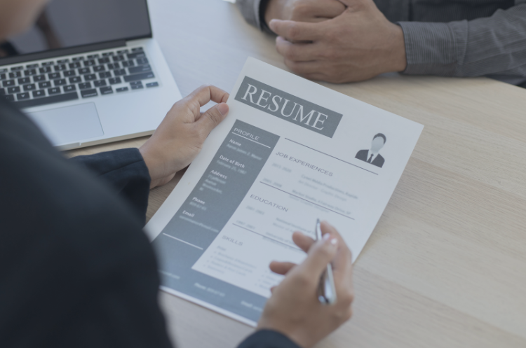 An over-the-shoulder view of a hiring manager reviewing a resume during a job interview with a candidate in a professional setting. This visual highlights career transitions, executive recruitment, and second career opportunities in Singapore, emphasizing the importance of a well-structured CV for experienced professionals pivoting into new industries.