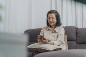 A mature woman in Singapore sitting on a couch, focused on her smartphone while exploring new opportunities. This image represents the digital transition, lifelong learning, and career planning for individuals over 60, highlighting the practical steps and resources available for seniors re-entering the workforce or starting a second career in Singapore.