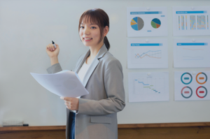 A smiling fractional executive in Singapore presenting data insights while standing next to a whiteboard with pie charts, sales trends, and performance metrics. This visual illustrates the role of on-demand leadership, strategic business consulting, and interim management, highlighting how companies in Singapore benefit from the high-level expertise of part-time senior leaders.