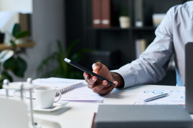 Professional using a smartphone at an office desk with business reports and documents, representing regional leadership, business operations, and executive decision-making.