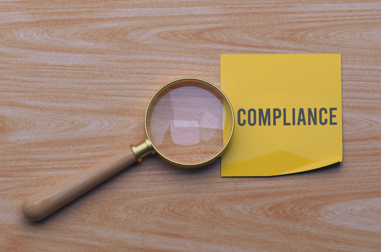Compliance consultant reviewing documents with a magnifying glass beside a compliance note.