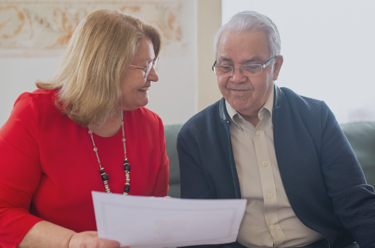 Senior couple sitting together on a sofa, smiling while reviewing documents, discussing opportunities for consulting after retirement.